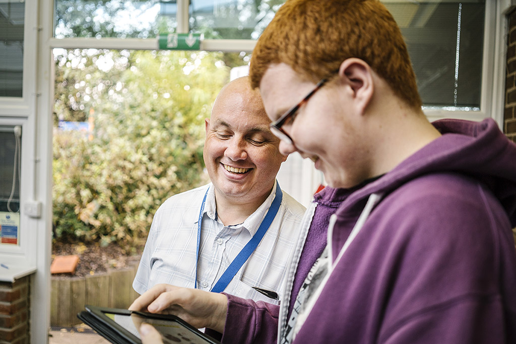 Young person looks at tablet with supporter